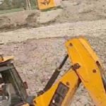 Neer - SIMBHAOLI SUGAR LIMITED Jadhopur Pond Project 2 - NEER Yellow backhoe loader at a rocky construction site with a worker in the cab operating the machine