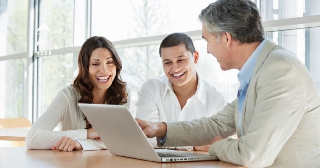 Three colleagues smiling and looking at a laptop during a meeting in a bright office.