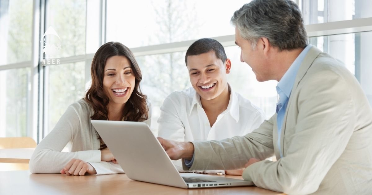 Three colleagues smiling and looking at a laptop during a meeting in a bright office.
